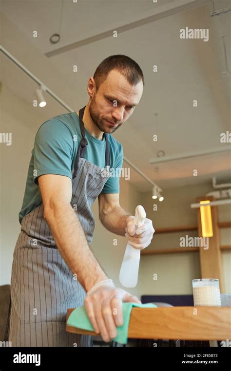 Vertical warm toned portrait of male waiter cleaning table in coffee ...