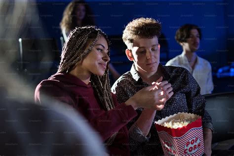 Cheerful Young Couple Eating Popcorn While Watching Movie In Cinema