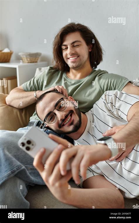 A Gay Couple Relaxes On A Couch One Laying With His Head In The Other S Lap As They Use A Phone