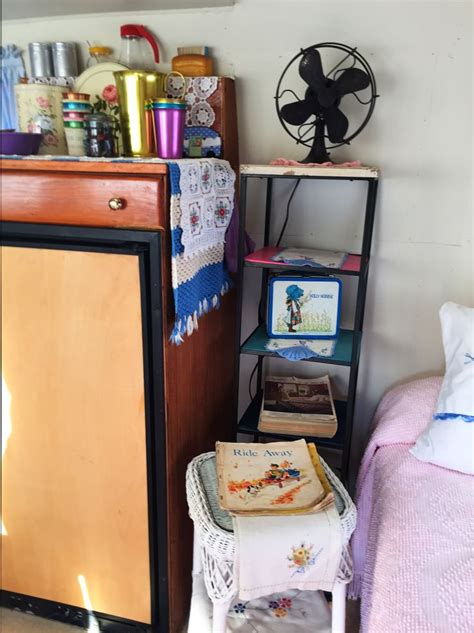 A Small Room With A Bed Fan And Other Items On The Shelf Next To It