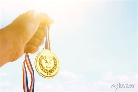 Homem mão levantada segurando a medalha de ouro contra o céu