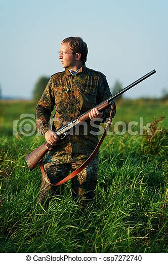 Hunter with rifle gun. Male hunter in camouflage clothes ready to hunt at lake bank with hunting ...