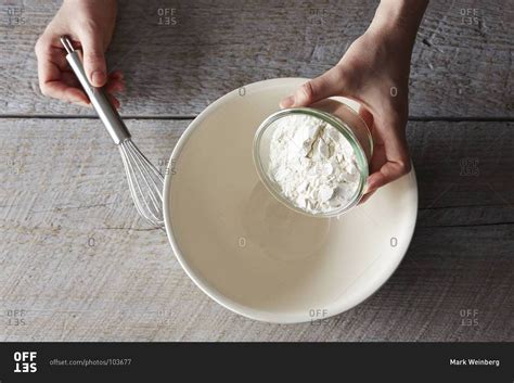 Top View Of Pouring Flour From A Small Glass Bowl Into A Larger White