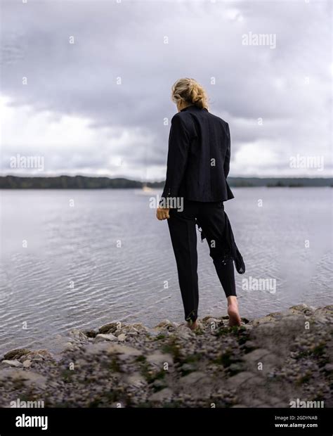 A Back View Of A Cool Barefoot Woman In A Black Suit Standing Near A