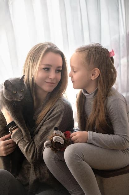 Mãe e filha estão sentadas em casa no sofá elas têm um lindo gato cinza