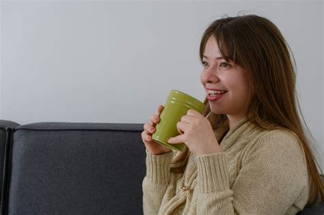 Joven latina tomando una taza de café mientras descansa en un sillón con ropa cómoda Foto Premium