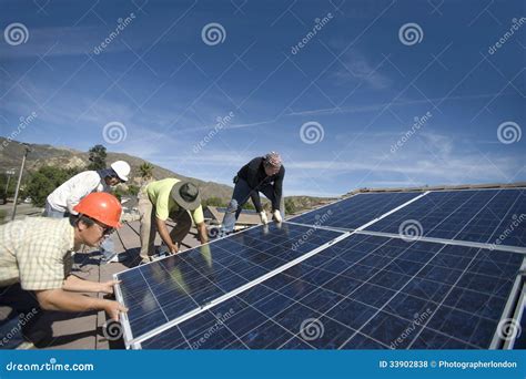 Engineers Lifting Heavy Solar Panel Against Blue Sky Stock Photo