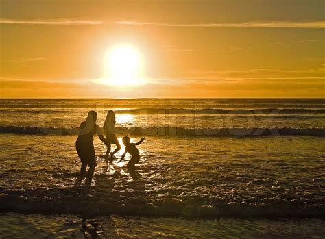 Silhuetter af børn der leger på stranden mod solnedgangen Stock foto