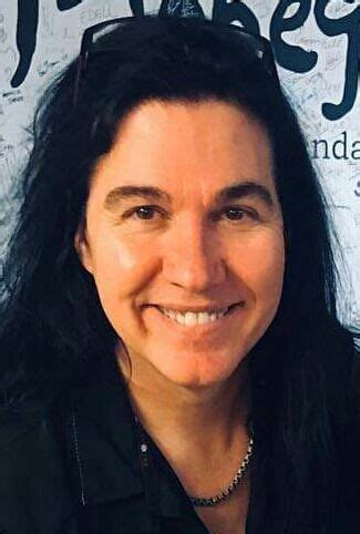 A Woman With Long Black Hair Smiling At The Camera While Standing In