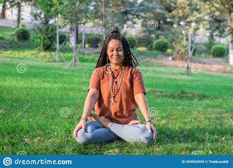 Young Woman Is Sitting In The Lotus Position And Meditating In A Park