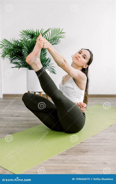 Pretty Caucasian Girl In Sport Clothes Performing Stretching Yoga Exercise Sitting On Green