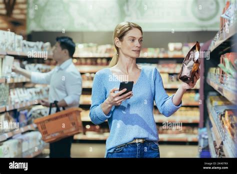 Eine schöne junge blonde Frau steht in einem Supermarkt Sie hält ein Telefon und eine Packung