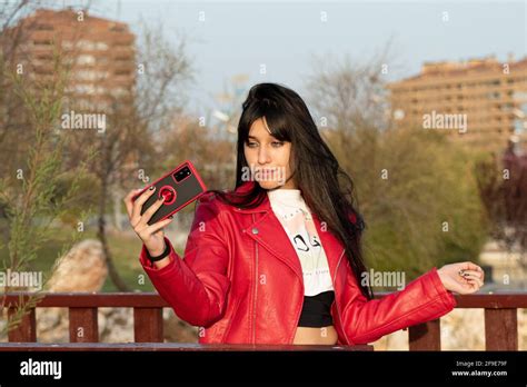 Green Eyed Latina Teen Taking A Selfie With Her Mobile In The Park With A Red Check Stock Photo