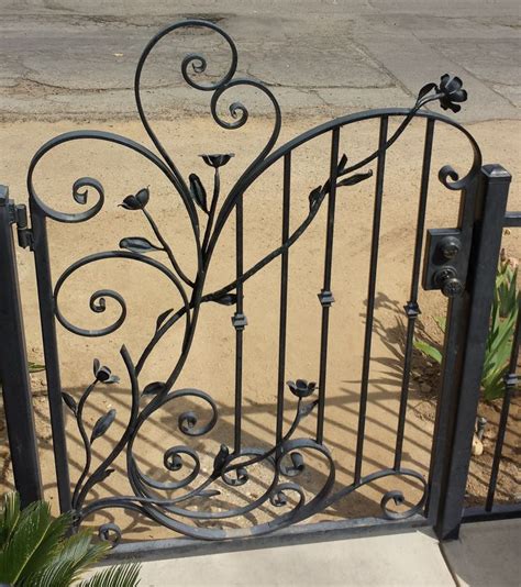 An Iron Gate With Flowers And Leaves On The Top In Front Of A Sidewalk