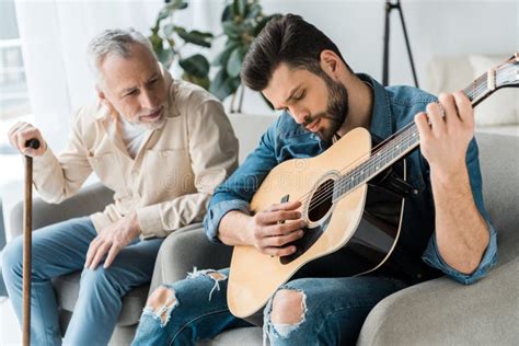 Bearded Man Playing Acoustic Guitar Near Happy Senior Father At Home