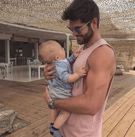 A Man Holding A Baby On Top Of A Wooden Deck In Front Of A Building