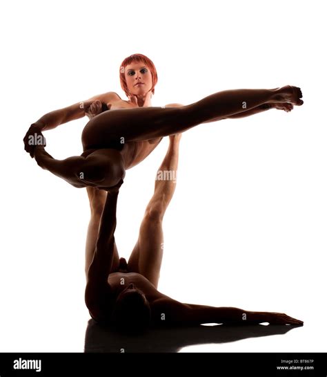 Studio Shot Of Carefully Lit Nude Male And Female Athletes Performing Acrobatic Yoga Against A