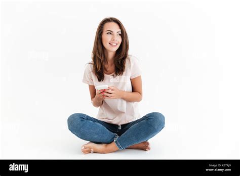 Pleased Brunette Woman Sitting On The Floor With Smartphone In Hands And Looking Away Stock