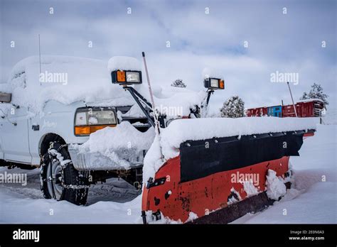 A white truck with a red snow plow and add on lights parked in the snow ...