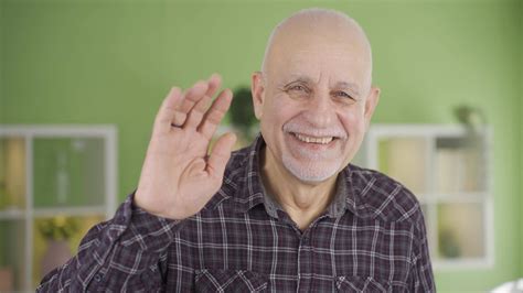 Sympathetic old man smiling looking at camera and waving, saying hello ...