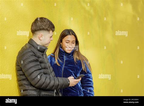 Boy Shows His Mobile Phone To A Latina Girl With A Yellow Wall In The Background Stock Photo Alamy