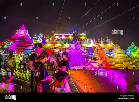 Tourists And Local Residents View Sand Sculptures Featuring Shape Of