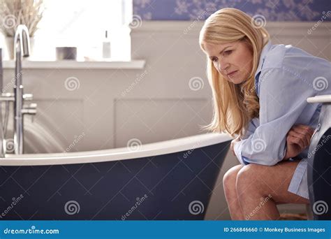 Menopausal Mature Woman Suffering With Incontinence Sitting On Toilet At Home Stock Photo