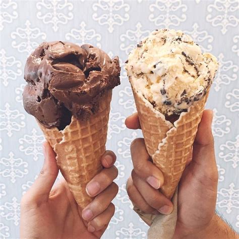 Two People Holding Up Ice Cream Cones With Chocolate And Oreo Toppings