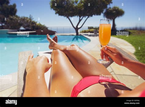 Young woman in bikini bronzée avec des jus de fruits assis sur une chaise de pont soleil proche