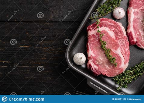 Raw Rib Eye Beef Steak With Pepper And Herbs On Black Wooden Table