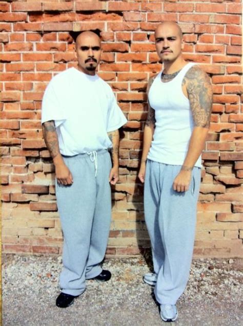 two men standing next to each other in front of a brick wall