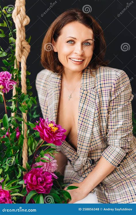 An Attractive Brunette Woman In A Plaid Jacket On A Swing With Peony Flowers Stock Photo