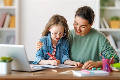 Niño y adulto felices están sentados en el escritorio Niña haciendo la ...