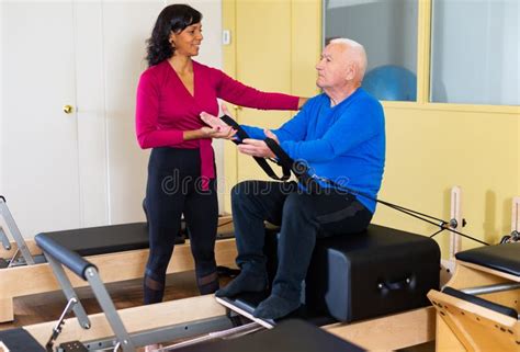 Senior Man Doing Pilates On Reformer With Hispanic Female Trainer Stock