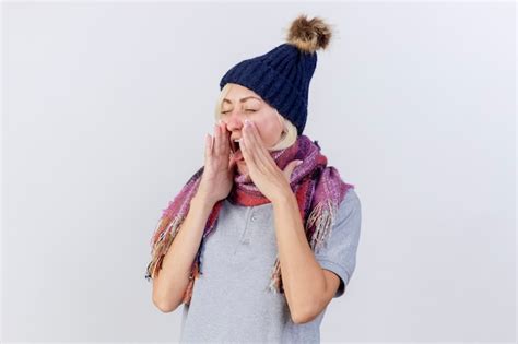 Agacé jeune blonde femme malade porter chapeau hiver et écharpe sort langue tenant