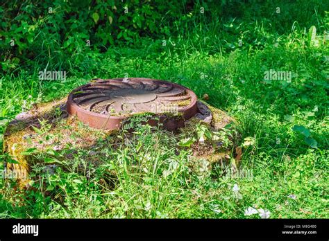 Cast Iron Cover On The Manhole Well Sewer Chamber Among The Green Grass