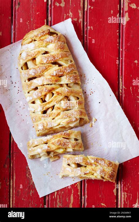 Apple Strudel On Parchment Paper With Two Slices Cut Off On A Red