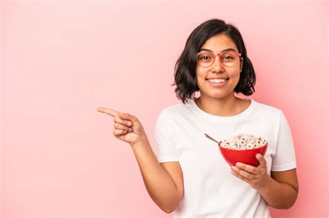 Mujer Latina Joven Sosteniendo Cereales Aislados Sobre Fondo Rosa Sonriendo Y Apuntando A Un