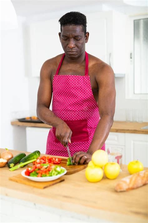 Man With A Naked Torso In An Apron Prepares A Vegetable Salad In The Kitchen Stock Photo Image
