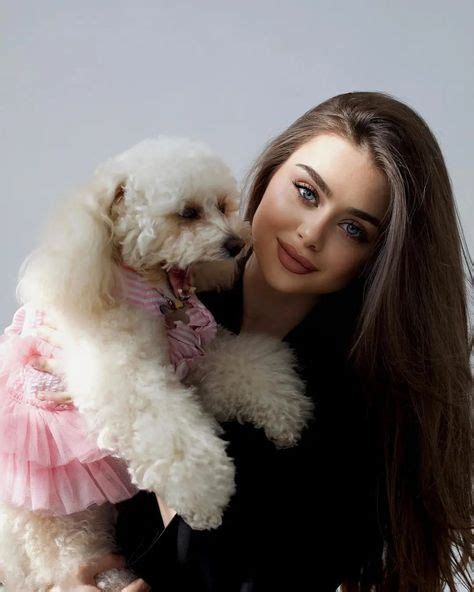 A Woman Holding A White Poodle In Her Arms And Wearing A Pink Dress