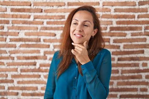Brunette Woman Standing Over Bricks Wall Looking Confident At The Camera Smiling With Crossed