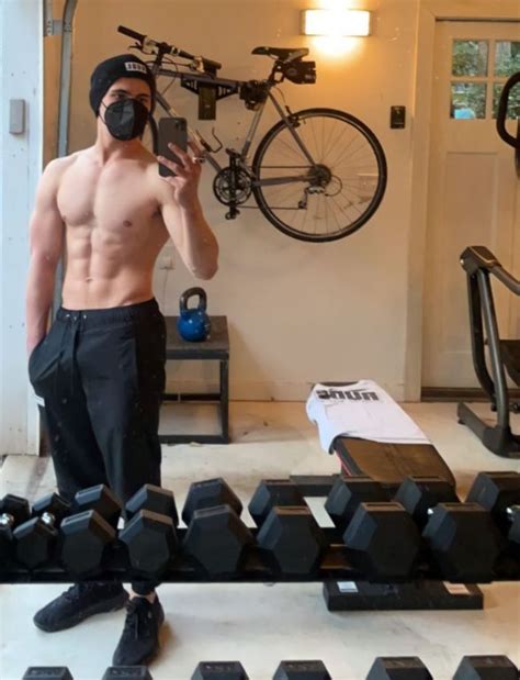 A Shirtless Man Taking A Selfie In Front Of A Bicycle And Gym Equipment