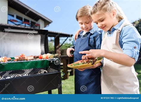 Children Testing Fresh Meat Just Cooked On Barbecue Grill Outdoors