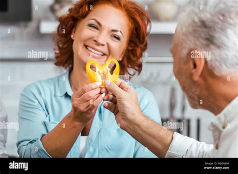 Happy Mature Couple Preparing Salad For Dinner And Making Heart From Bell Pepper Pieces At Home