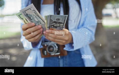 Hispanic Brunette Woman Counting Us Dollar Bills While Standing Outdoors In A Park Holding A