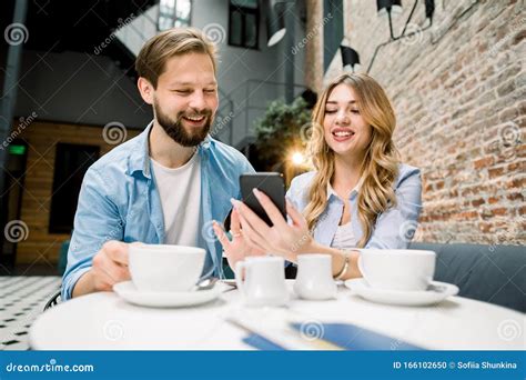 Happy Couple Sitting At The Table Drinking Coffe Or Tea Watching