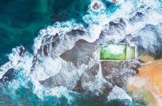 An Aerial View Of The Ocean And Beach With Green Grass In The Water