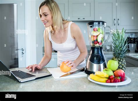 Pretty Blonde Woman Preparing A Smoothie With Recipe On Laptop Stock