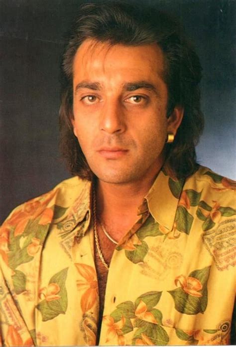 a man with long hair wearing a yellow flowered shirt and gold hooprings