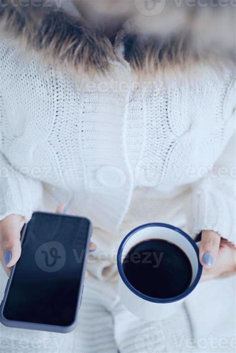 Top View And Close Up Woman Hands Holding Hot Cup Of Coffee And Smartphone In Cold Weather